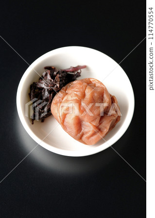 Aerial view of red shiso and pickled plums served on a small plate on a black background 114770554