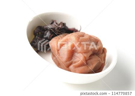 Red shiso and pickled plums served on a small white round plate photographed on a white background 114770857