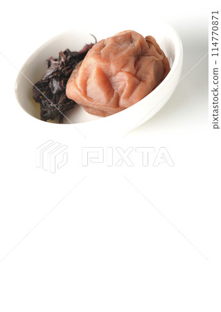 Red shiso and pickled plums served on a small white round plate photographed on a white background 114770871