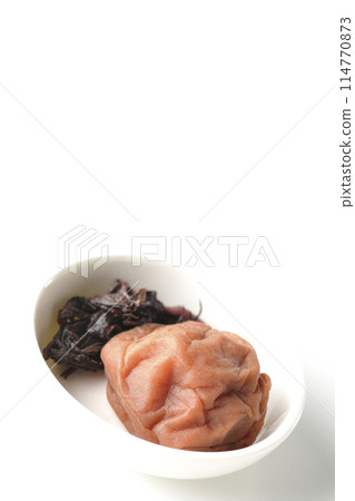 Red shiso and pickled plums served on a small white round plate photographed on a white background Red shiso and pickled plums served on a small white round plate photographed on a white background 114770873