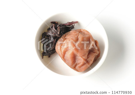 Aerial view of red shiso and pickled plums served on a small white round plate on a white background Aerial view of red shiso and pickled plums served on a small white round plate on a white background 114770930