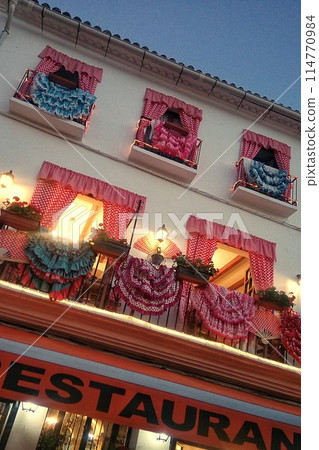Cafe on typical old town street with dress decorated windows face. Spanish architecture of Plaza de los Naranjos in Marbella, Costa del Sol, Andalucia, Spain. Marbella, Spain - June 23, 2016 Cafe on typical old town street with dress decorated windows face. Spanish architecture of Plaza de los Naranjos in Marbella, Costa del Sol, Andalucia, Spain. Marbella, Spain - June 23, 2016 114770984