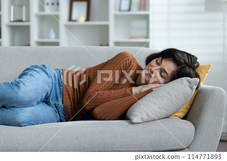 Young woman peacefully sleeping on a grey sofa in a cozy living room setting, showcasing relaxation and comfort in a homely environment. Young woman peacefully sleeping on a grey sofa in a cozy living room setting, showcasing relaxation and comfort in a homely environment. 114771893