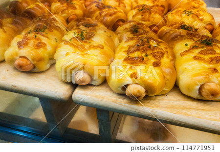 Close-up sausage bun on the shelf with warm light in the bakery store. Close-up sausage bun on the shelf with warm light in the bakery store. 114771951