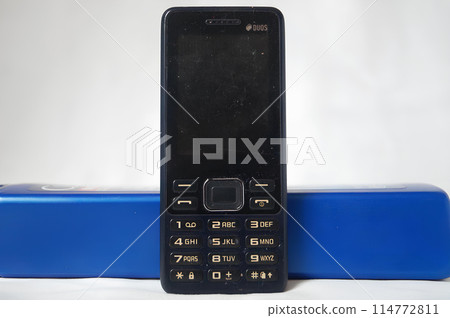 A black flip phone sits on a blue object A black flip phone sits on a blue object 114772811