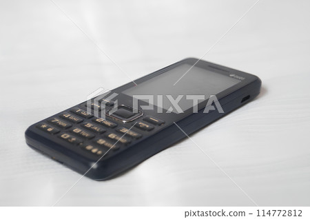 A black flip phone is laying on a white surface A black flip phone is laying on a white surface 114772812