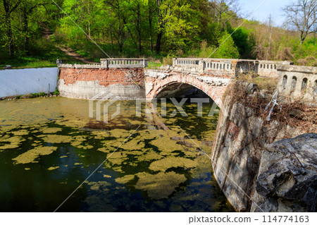 Old arched brick bridge across a pond in Sharovka Palace park in in Kharkov region, Ukraine 114774163
