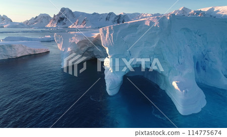 Huge icebergs blue cave, melting glacier in Antarctica. Large mass of ice floating polar ocean water. Snow covered mountains in pink sunset light. Antarctica travel, Arctic landscape. Drone flight Huge icebergs blue cave, melting glacier in Antarctica. Large mass of ice floating polar ocean water. Snow covered mountains in pink sunset light. Antarctica travel, Arctic landscape. Drone flight 114775674