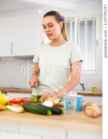 Smiling young woman preparing vegetable salad in home kitchen 114776147