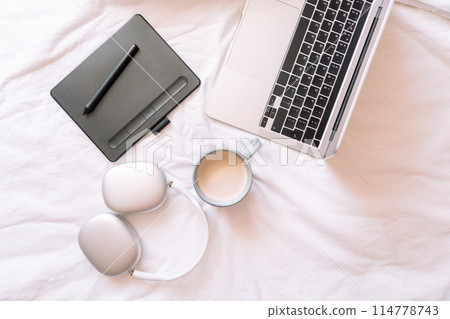 Cozy workplace with wireless headphones and laptop with a cup of coffee and graphics tablet Cozy workplace with wireless headphones and laptop with a cup of coffee and graphics tablet 114778743