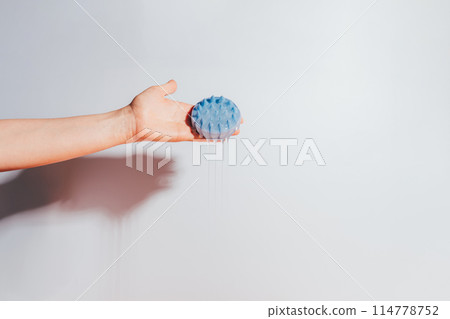 Hand holding a blue massager for the scalp and shampoo flows from it 114778752