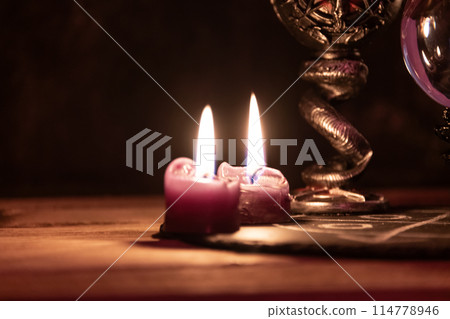 A detailed close-up shot of two lit pink candles with a dark, mystical background, emphasizing a ritualistic theme. 114778946