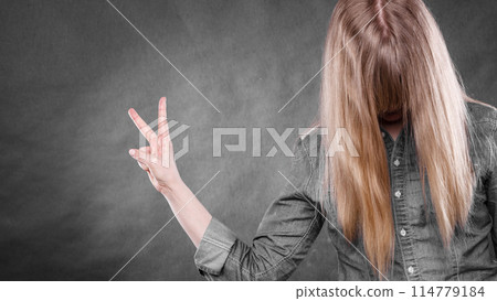 Blonde woman with covered face showing victory symbol. 114779184