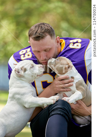 American football player with a dog posing on camera in a park. Copy space, sports banner. Concept american football, sport for the protection of animals. 114780034
