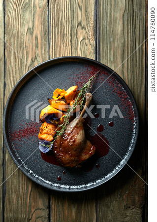 Roasted duck leg with confit pumpkin, closeup. Horizontal top view, top shot. Copy space, wooden background, low key Roasted duck leg with confit pumpkin, closeup. Horizontal top view, top shot. Copy space, wooden background, low key 114780090