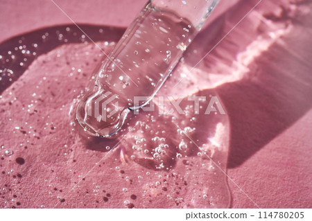 Pipette with serum shimmering in the sun on a pink background. 114780205