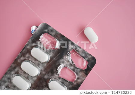 Open pack of pills on a pink background. 114780223