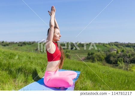 Young yogi woman meditating in lotus pose sitting on the mat at green hill 114781217