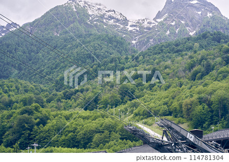 The mechanisms of the cable car are high against the background of snow-capped mountains. The concept of active recreation and tourism. A beautiful landscape with space to copy. High quality photo 114781304