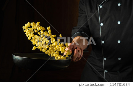 The chef prepares pasta in a frying pan for lunch. Italian cuisine or shell-type pasta. Advertising space on a dark background The chef prepares pasta in a frying pan for lunch. Italian cuisine or shell-type pasta. Advertising space on a dark background 114781684
