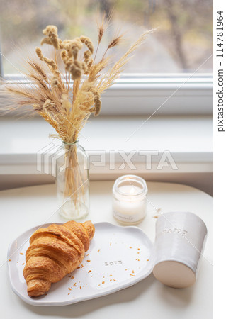 White glass and a plate on which lies a croissant made of clay with the inscription love, handmade. 114781964