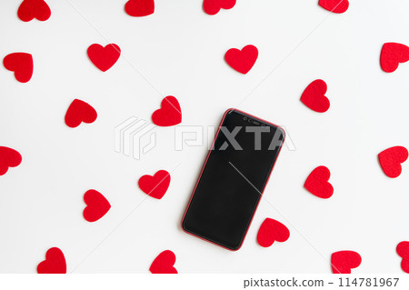 Smartphone surrounded by red felt hearts on a white background. Place for an inscription. 114781967