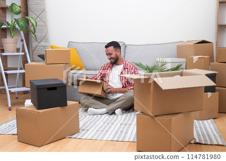 Young male with beard sits in new house unpacking things brought by courier in large cardboard boxes finding decorative items from old apartment with pleasant memories 114781980