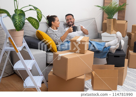 Unpacking and moving day become a celebration as a young couple cheers with coffee cups on the sofa, surrounded by boxes, making their new house their own Unpacking and moving day become a celebration as a young couple cheers with coffee cups on the sofa, surrounded by boxes, making their new house their own 114781990
