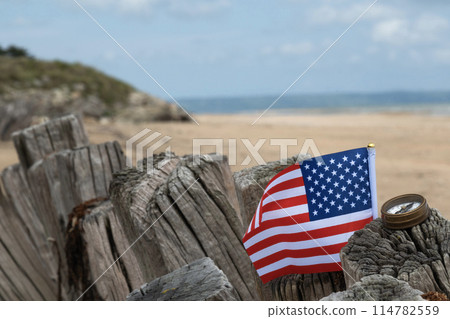 Utah Beach WWII with Flag of USA and compass in sharp focus with beach and ocean in background. Sandy beach and fence posts. Normandy France rememberance of Veterans Day. High quality photo Utah Beach WWII with Flag of USA and compass in sharp focus with beach and ocean in background. Sandy beach and fence posts. Normandy France rememberance of Veterans Day. High quality photo 114782559