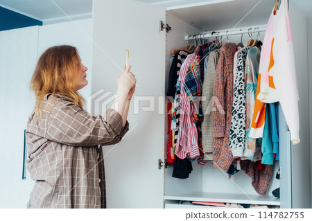 Woman taking photo of the sweater using her smartphone for selling or donating her clothes. Decluttering , Sorting Clothes, And Cleaning Up wardrobe. Reuse, second-hand concept. Conscious consumer. 114782755