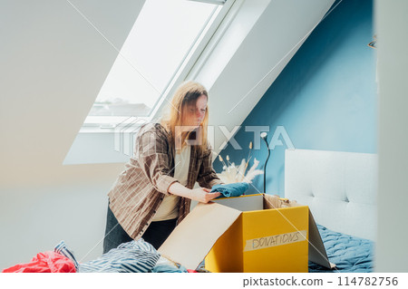Woman selecting clothes from her wardrobe for recycling, donating to a Charity shop. Decluttering, Sorting clothes, Cleaning Up. Reuse, second hand concept. Conscious consumer, sustainable lifestyle. 114782756
