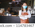 Portrait of Asian woman barista wearing face mask in coffee shop 114783467