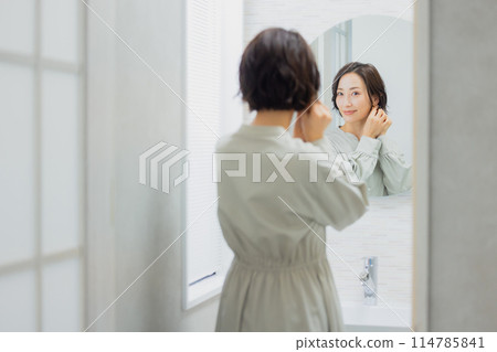 A woman looking at a mirror in the washroom 114785841