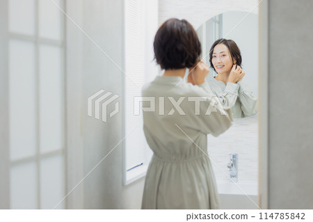 A woman looking at a mirror in the washroom 114785842