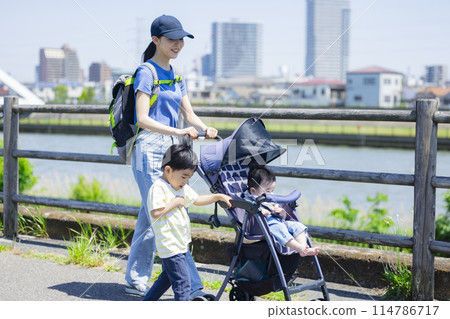 A parent and child walking along the river bank pushing a stroller 114786717
