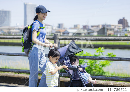 A parent and child walking along the river bank pushing a stroller 114786721