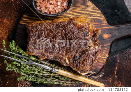 Roast Striploin beef meat steak or club steak on a wooden board with herbs. Dark background. Top view Roast Striploin beef meat steak or club steak on a wooden board with herbs. Dark background. Top view 114788152