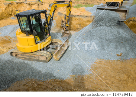 Construction sites require an excavator to fill irregularities with granite rubble base that serves as foundation for concrete Construction sites require an excavator to fill irregularities with granite rubble base that serves as foundation for concrete 114789412