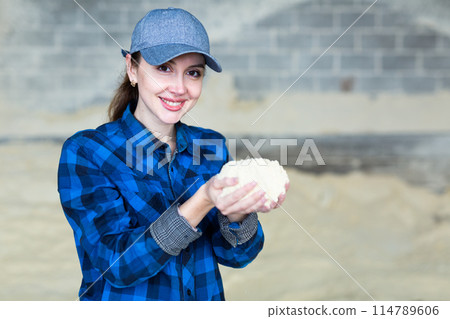 Woman checks the quality of cornmeal in an animal feed warehouse 114789606