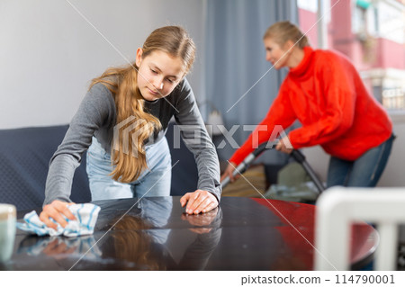 Teenage girl cleaning table with rag 114790001