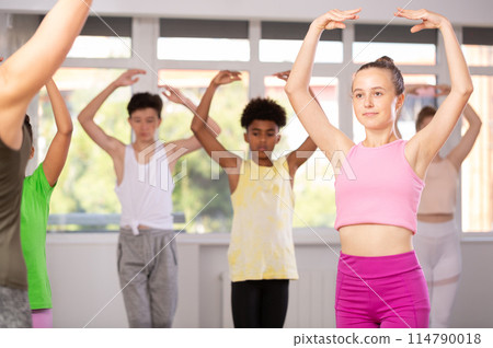 Positive teenage girl practicing ballet positions standing in row with others Positive teenage girl practicing ballet positions standing in row with others 114790018