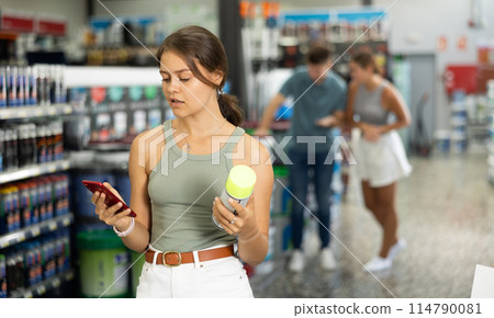 Girl scans QR code with her phone to check product information. Buying cans of aerosol paint at hardware shop Girl scans QR code with her phone to check product information. Buying cans of aerosol paint at hardware shop 114790081