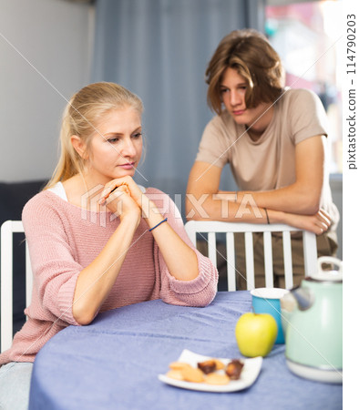 Upset woman sitting at home after disagreements with teenage son Upset woman sitting at home after disagreements with teenage son 114790203