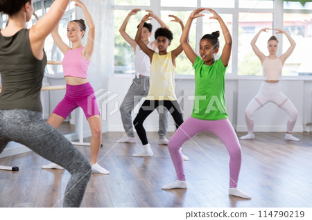 Thin teenage girl practicing plie position of ballet standing in row with others Thin teenage girl practicing plie position of ballet standing in row with others 114790219