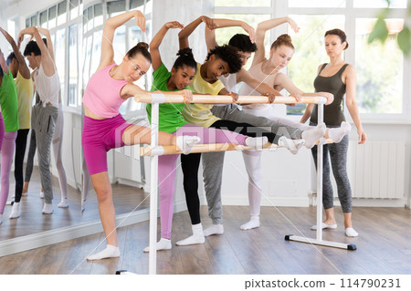 Teenage girl doing leg stretching exercise holding by ballet barre during dance courses 114790231