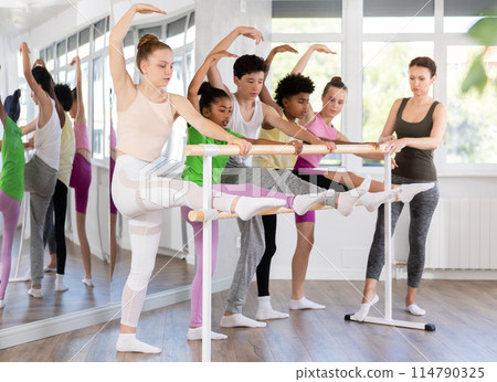 Teenage girl doing leg stretching exercise holding by ballet barre during dance courses Teenage girl doing leg stretching exercise holding by ballet barre during dance courses 114790325