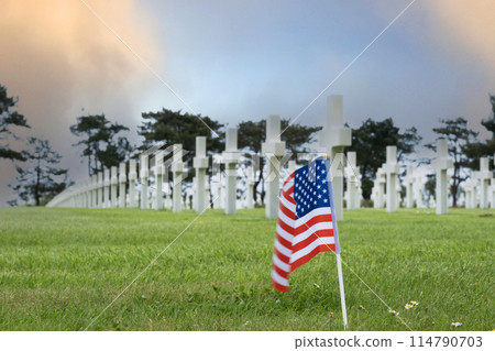 American cemetery at Normandy area. WWII memorial. Lines of grave stones with american flag. moring glow in blue sky and clouds. High quality photo 114790703