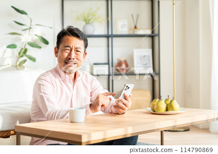 A middle-aged man operating a smartphone at home. 114790869