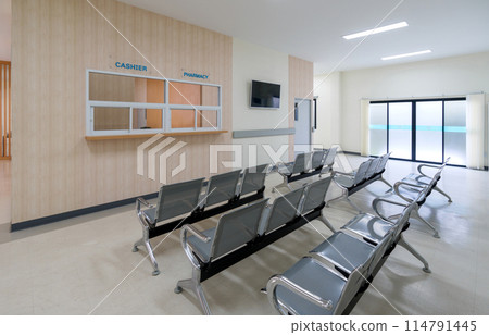 An empty waiting area with chairs, a cashier sign, and a pharmacy window in a modern building. There are rows of connected grey seating for individual waiting. Glass door on the right lead to the exit An empty waiting area with chairs, a cashier sign, and a pharmacy window in a modern building. There are rows of connected grey seating for individual waiting. Glass door on the right lead to the exit 114791445