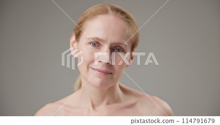 Anti age, Beauty, health and dry skin care concept - beautiful middle-aged mature Caucasian woman in her 50s touching her face skin and looking at the camera with a slight smile 114791679